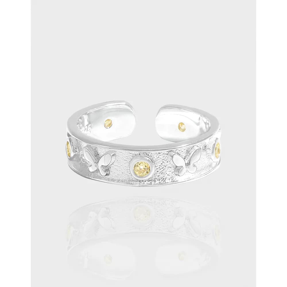 Close-up of a wide sterling silver ring with a textured band, butterfly motifs and small yellow stones.