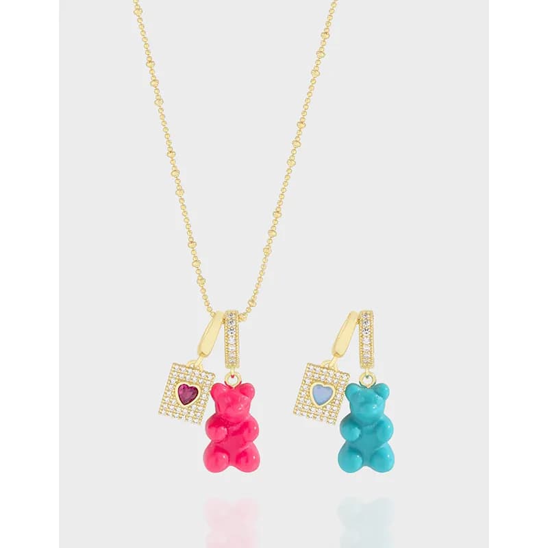 Gold-tone necklace with enamel gummy bears and a pavé heart-square pendant on a light background.