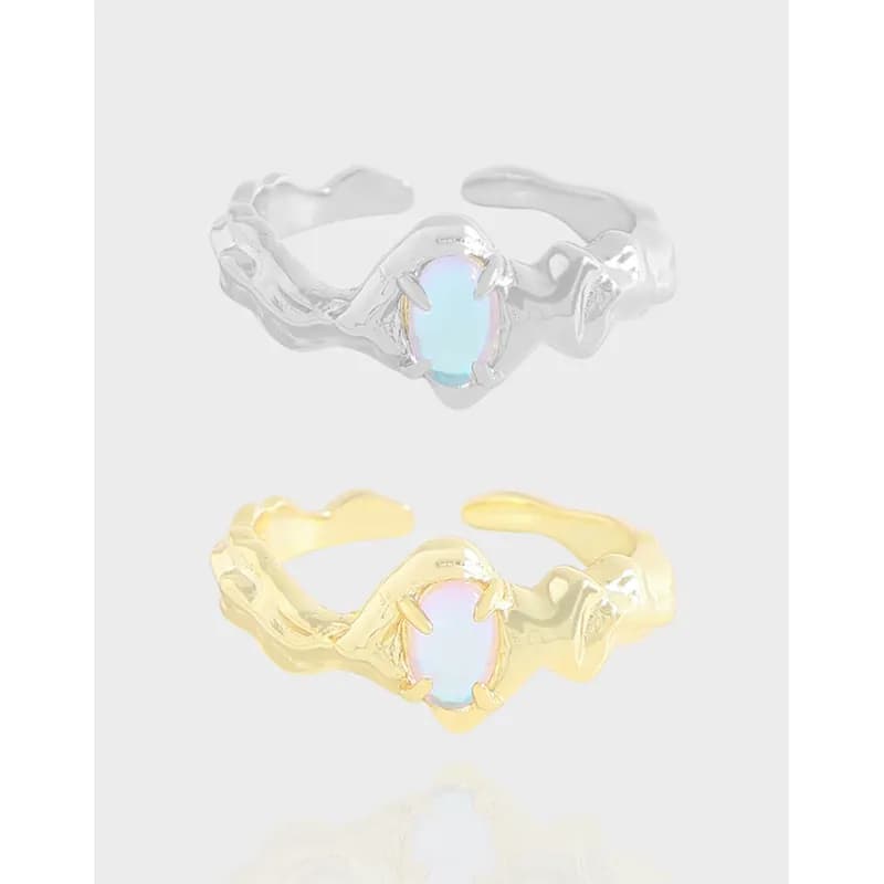 Two rings with oval opalescent stones in claw settings, one in silver and one in gold-tone, on a light background.