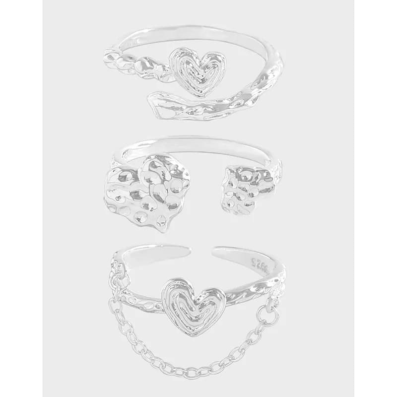 Stack of three polished sterling silver rings with heart motifs, shown together on a light background.