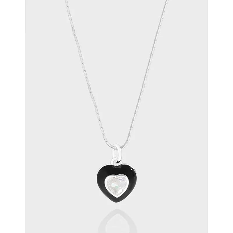 Close-up of a silver necklace with a black enamel heart pendant containing a small iridescent inner heart