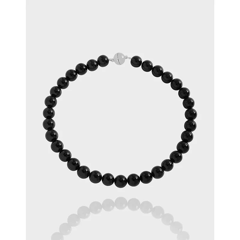 Polished black bead necklace with a silver clasp displayed on a light background.