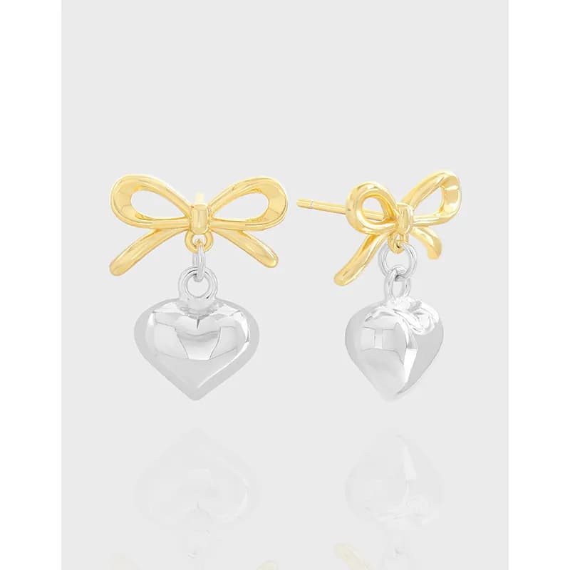 Two-tone bow earrings with dangling silver heart charms on polished gold-tone bows.