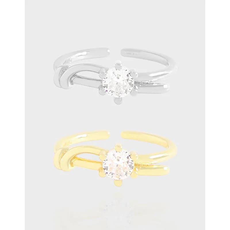 Polished split-band solitaire rings in silver and gold-tone with a central round stone on a light gray background.