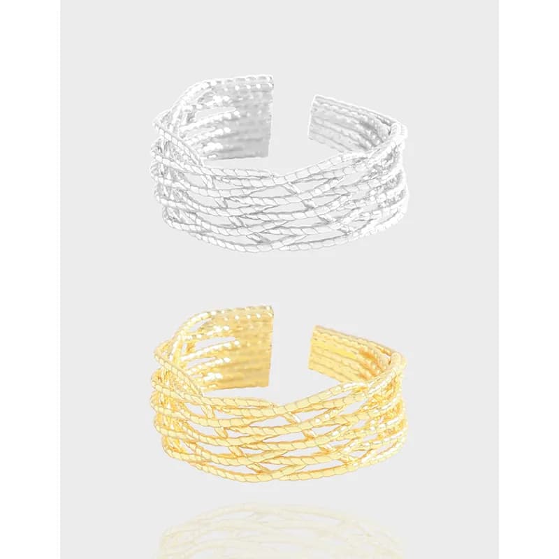 Open multi-strand braided ring in silver and gold-tone finishes displayed against a light gray background.