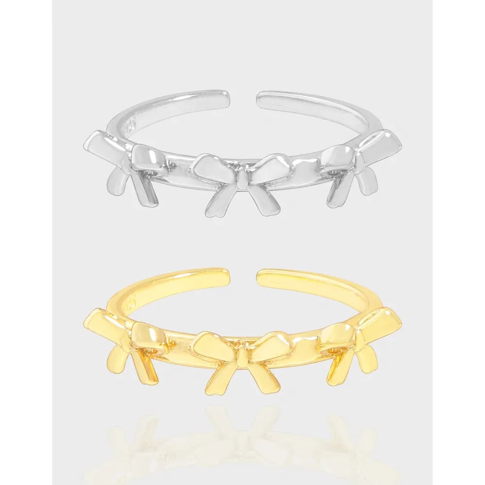 Polished open-band ring with bow-shaped links in silver and gold finishes displayed on a light background.