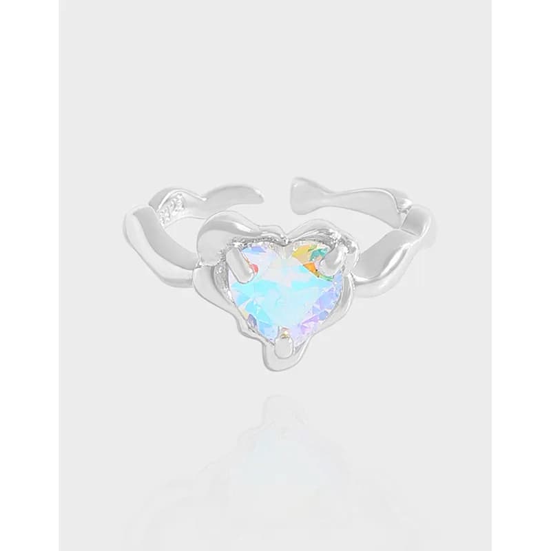 Polished sterling silver ring with a heart-shaped iridescent gemstone at the center on a pale background.