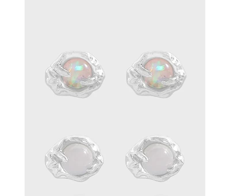Four stud earrings with irregular silver halos around round cabochons; two opal-like and two pale stones.