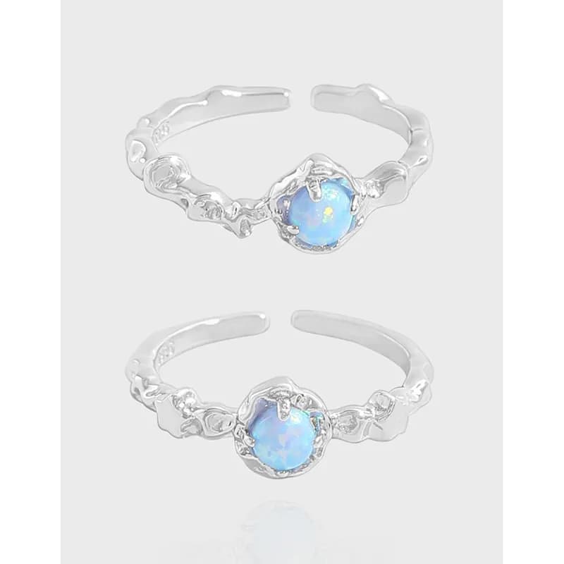 Polished sterling silver ring with a blue opal-like stone and ornate floral band on a neutral background.