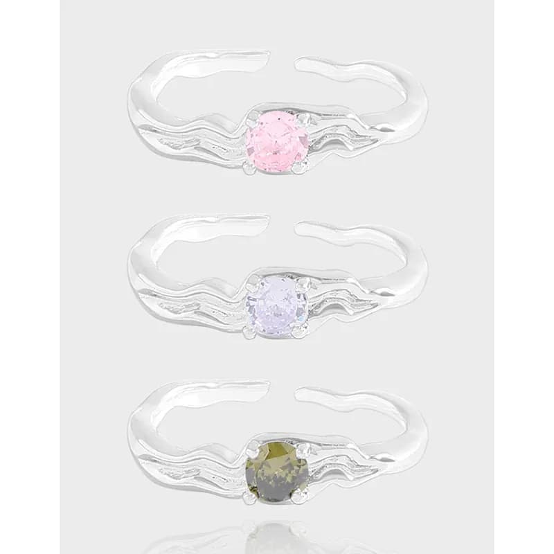 Three polished sterling silver rings with wavy bands and pastel round stones in pink, lavender, and olive hues.