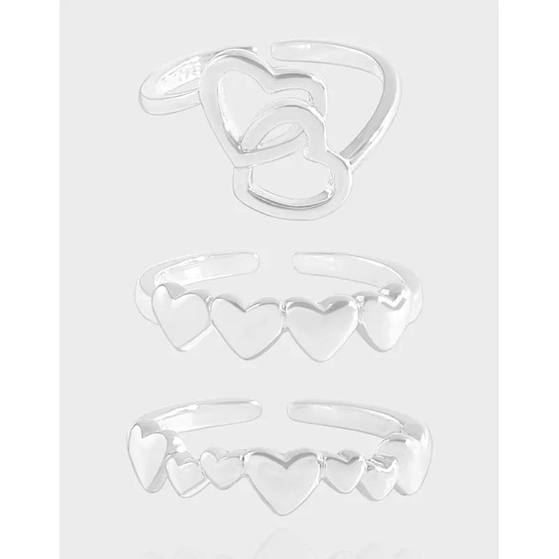 Polished sterling silver rings featuring interlocking and heart-shaped designs on a light background.