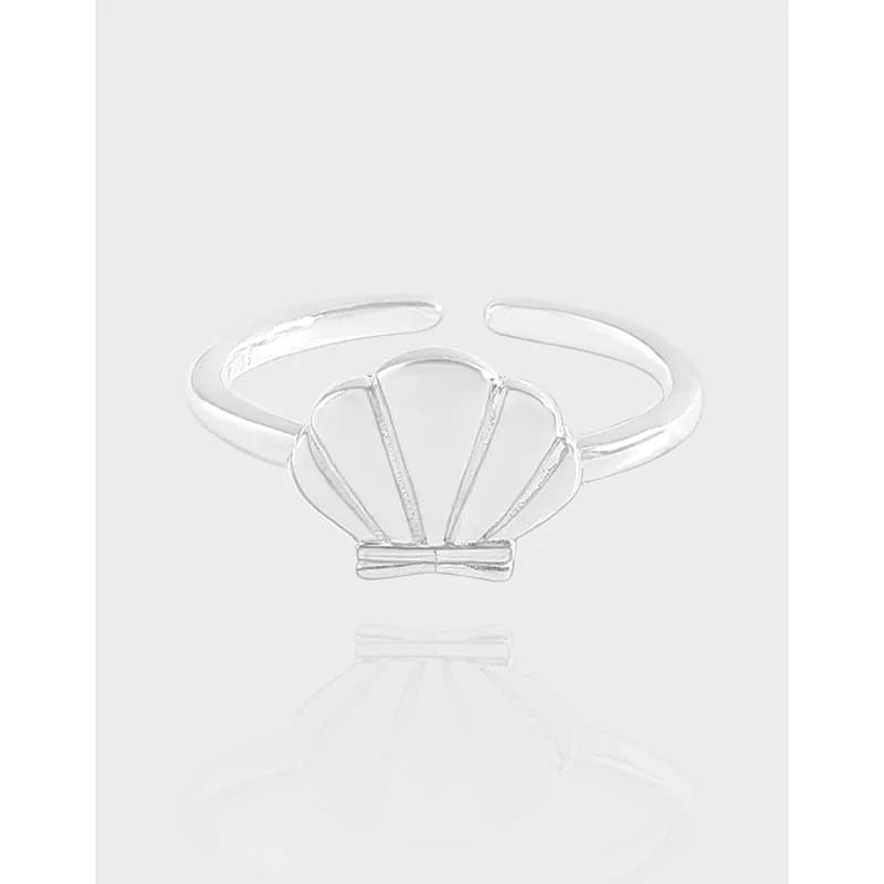 Open sterling silver ring with a shell motif on a pale background, shown from the front.