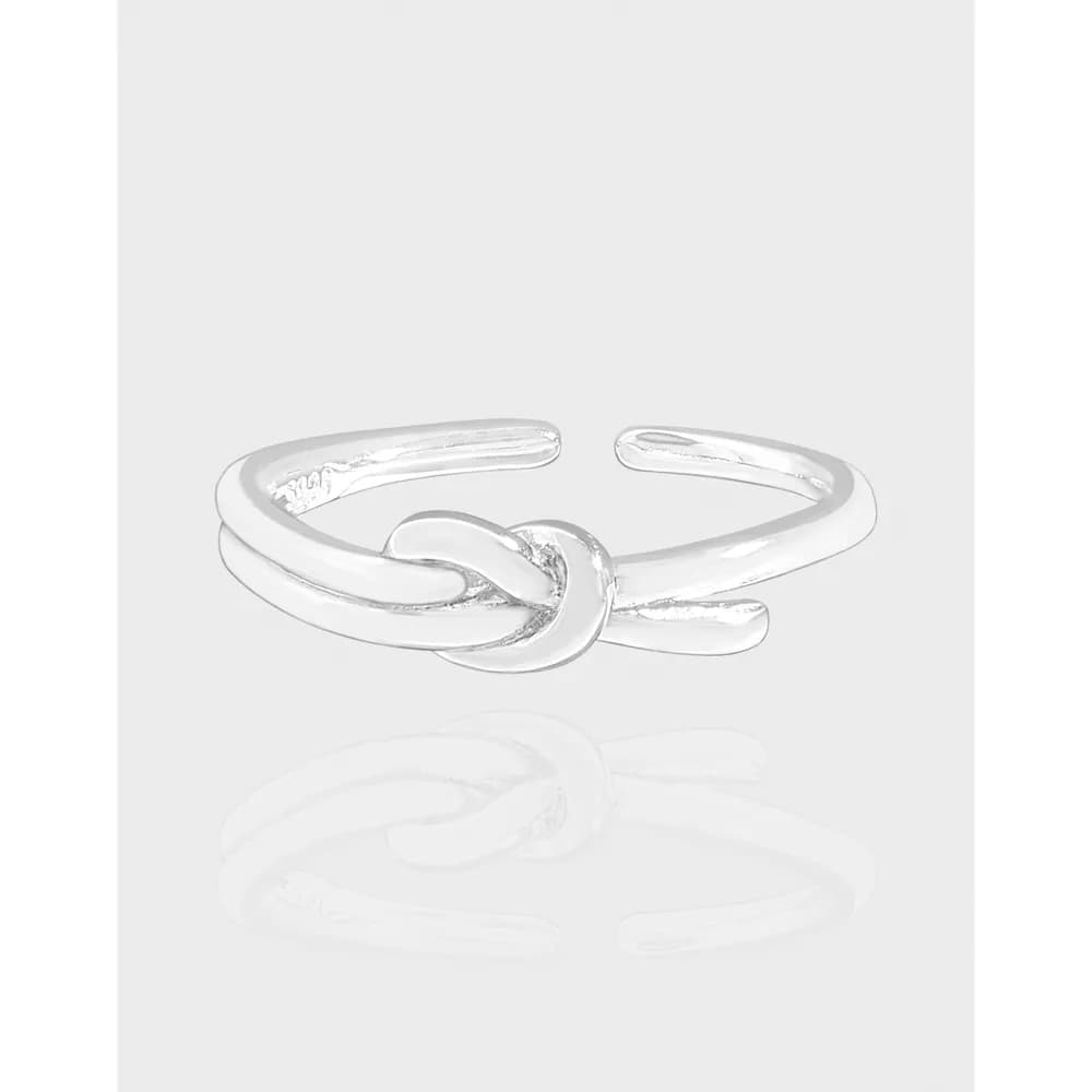 Polished sterling silver open-ring with a central knot detail on a light backdrop.