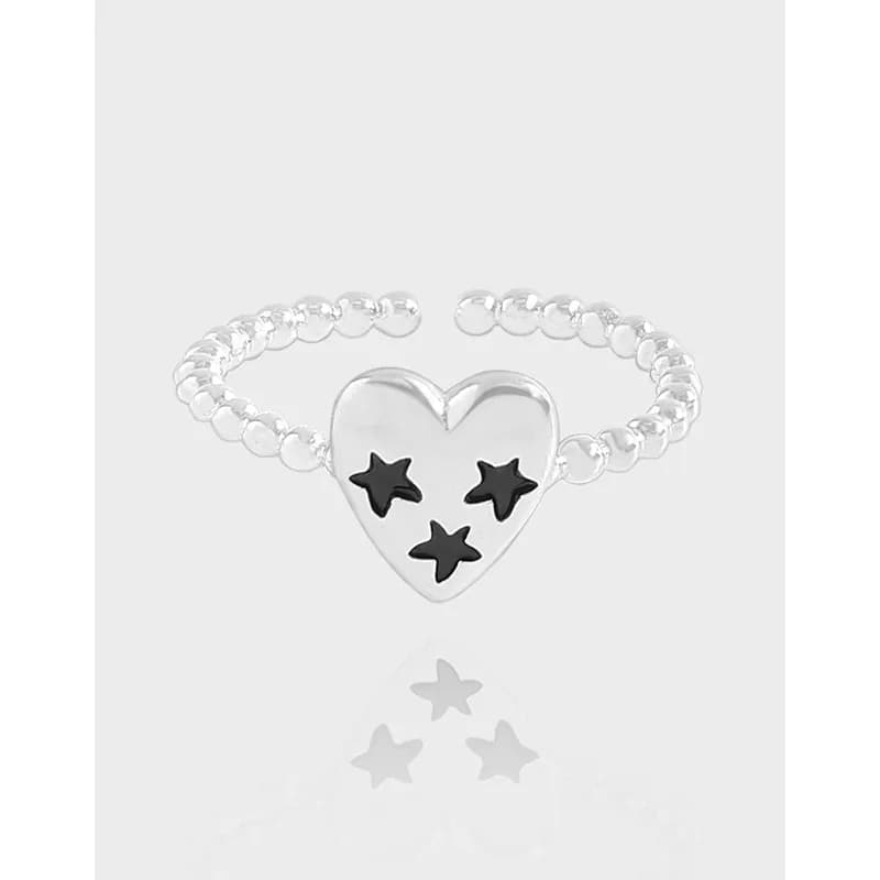 Polished sterling silver heart ring with three black star cutouts and a beaded band on a light background.