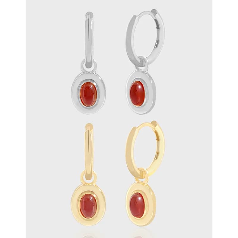 Polished silver and gold-tone oval red stone drop earrings with circular bezel set in hoops.