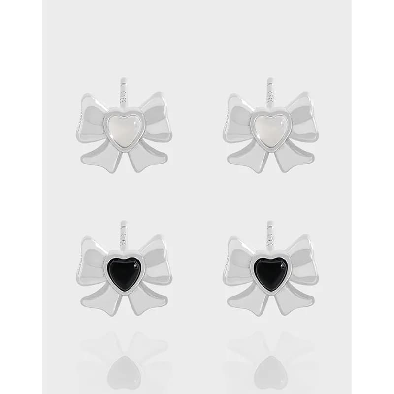 Four polished sterling silver bow-shaped earrings with heart centers shown on a light gray background.