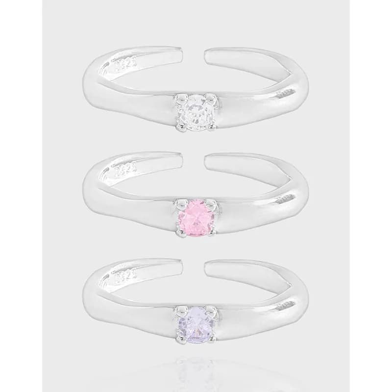 Three curved sterling silver rings with solitaire stones in clear, pink, and lavender, shown stacked on a light background.