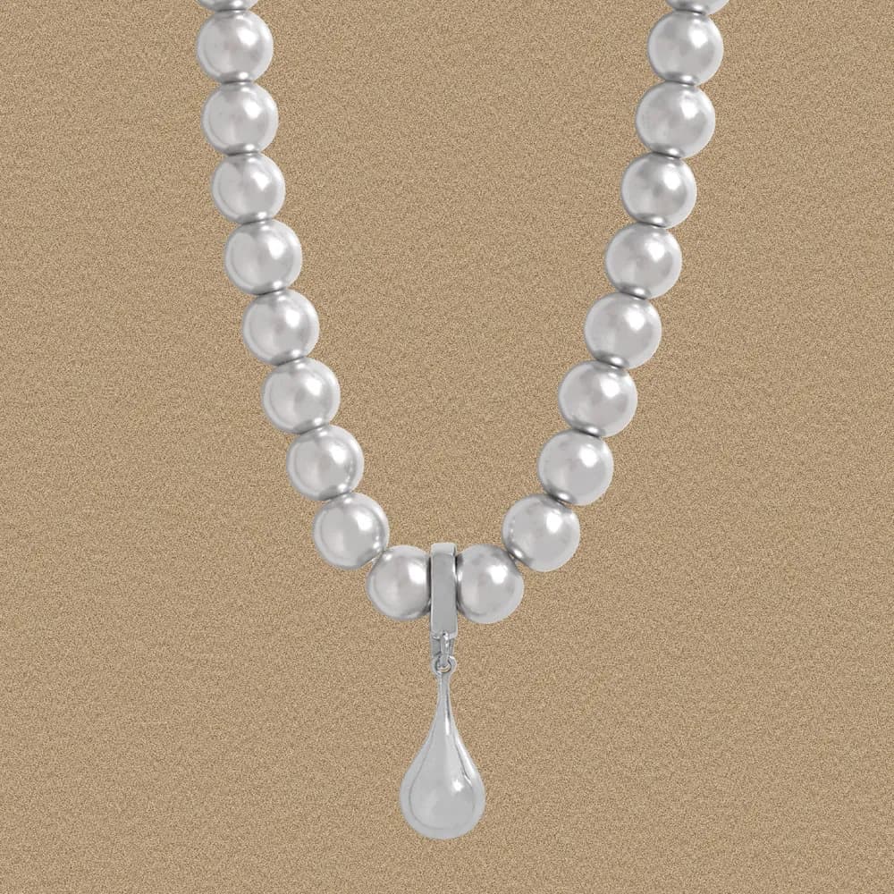Polished sterling silver bead necklace with a teardrop pendant against a beige background.