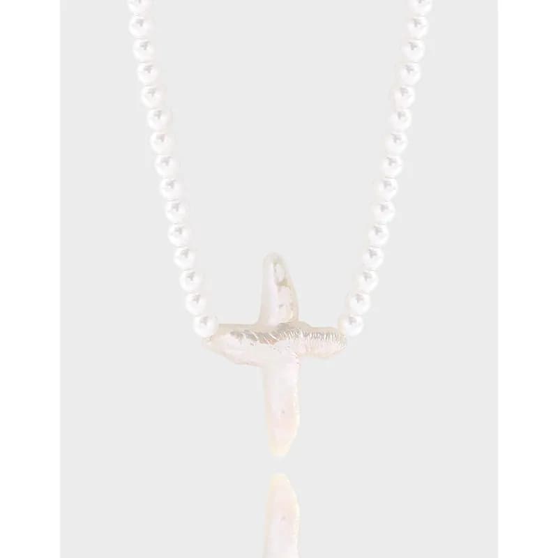 Pearl bead necklace with a small textured cross pendant on a slender chain.