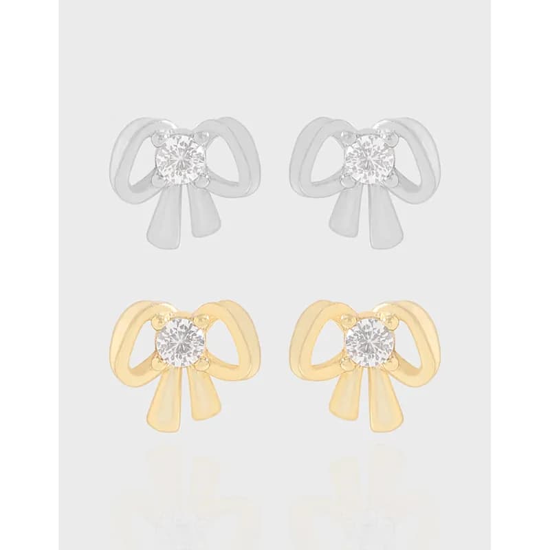 Pair of bow-shaped stud earrings in silver and gold-tone with a central clear stone