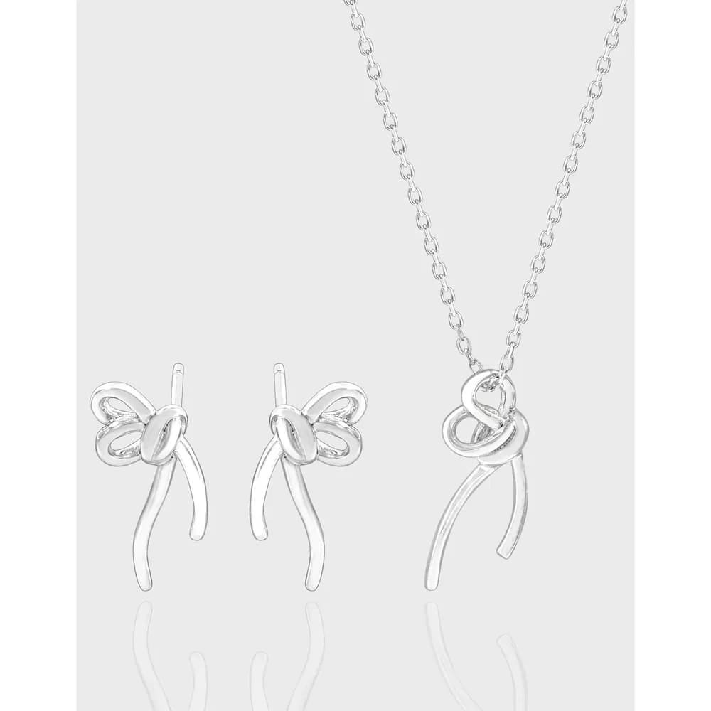 Polished sterling silver bow motif earrings and pendant on a fine chain set against a light background.