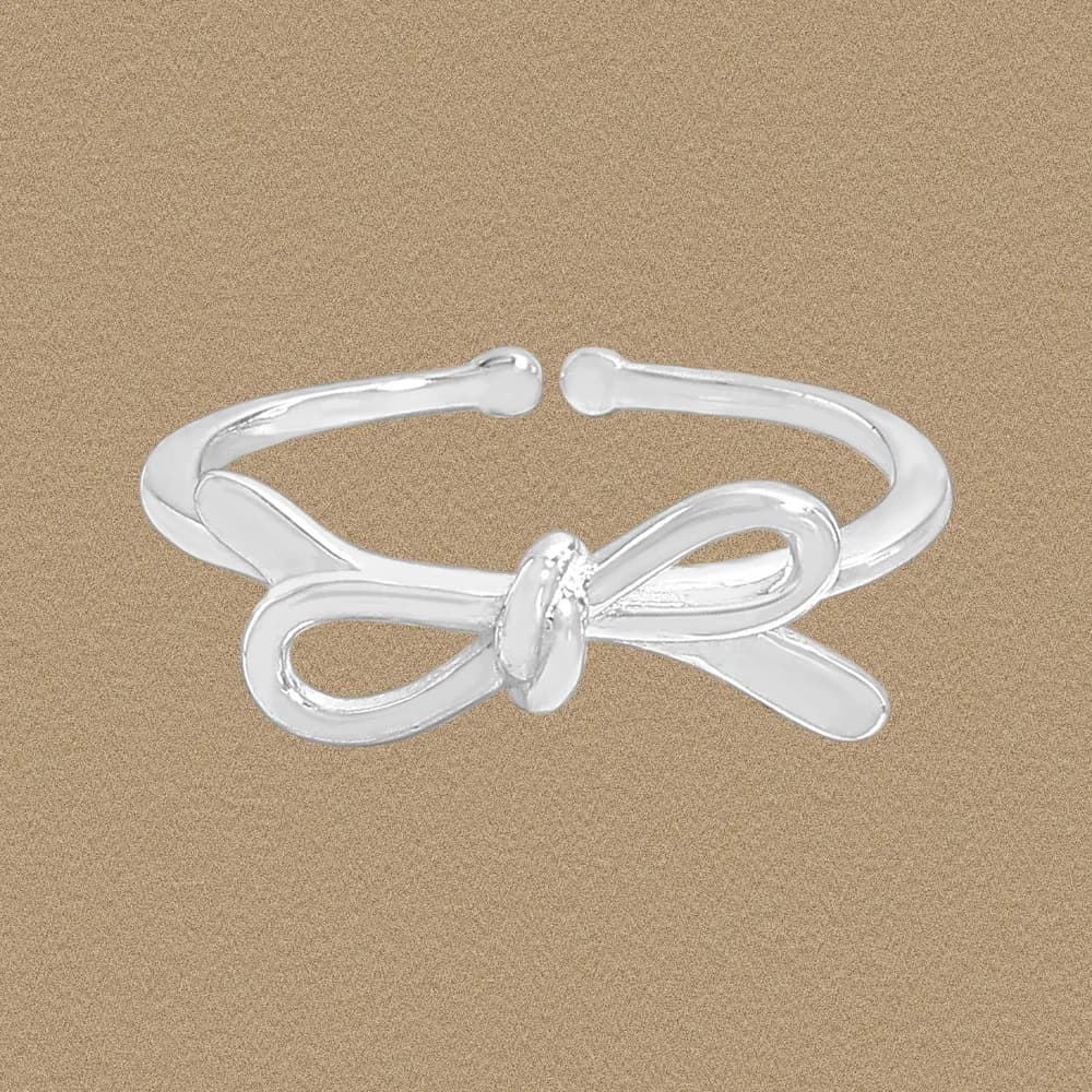 Polished sterling silver knot bow ring on a warm beige background.