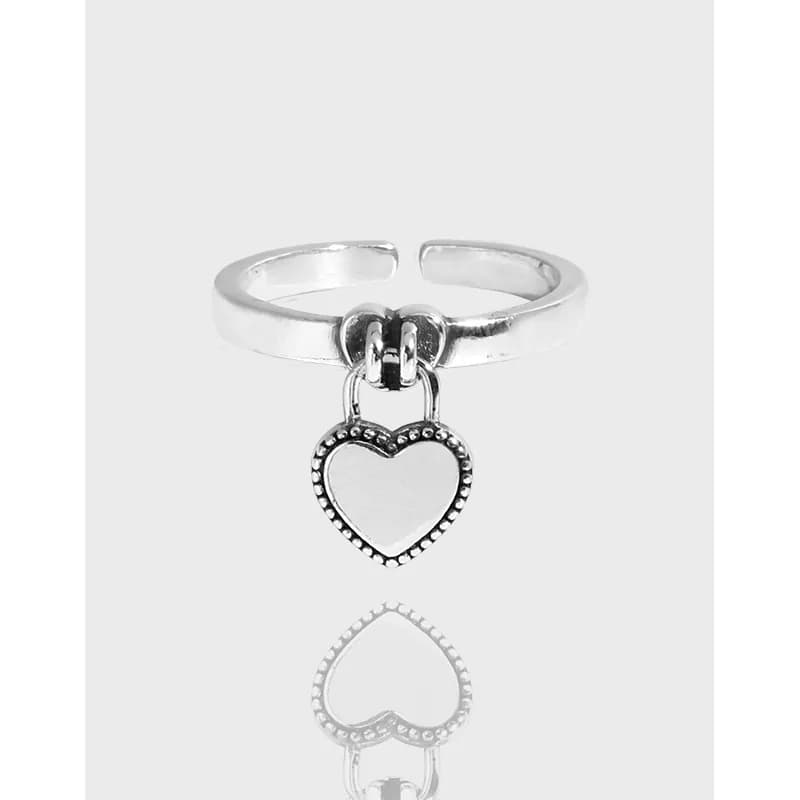 Open sterling silver ring with a hanging heart charm on a matte finish band.
