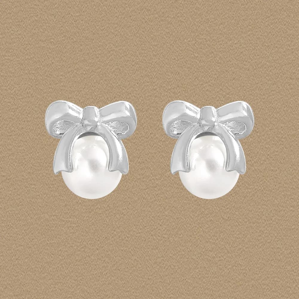 Pair of polished silver bow-shaped earrings with pearl drops on a neutral background.