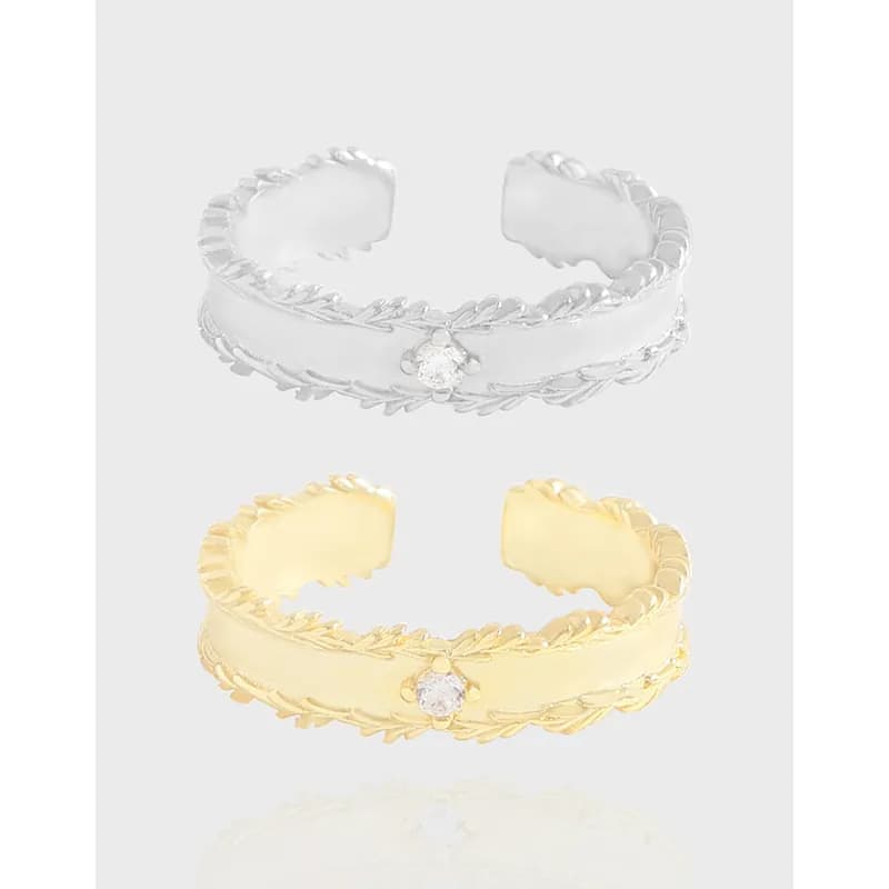 Polished open ring with braided leaf edge and small central gemstone, shown in silver and gold-tone finishes.