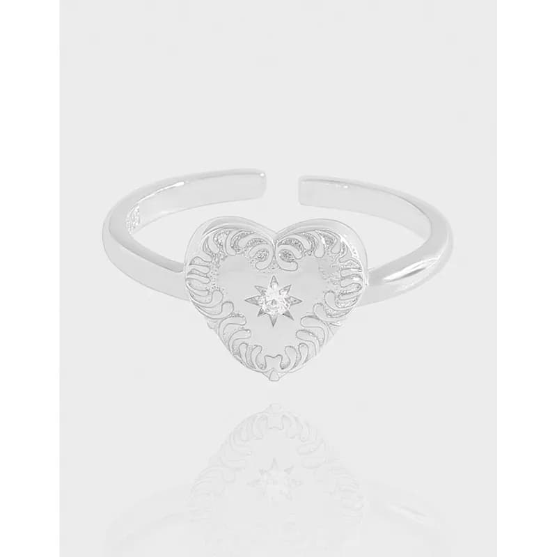 Polished sterling silver heart filigree ring with a small central stone and an adjustable open band.
