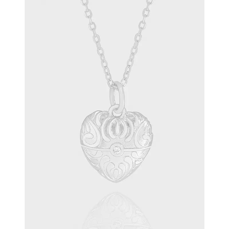 Close-up of a polished sterling silver heart pendant with filigree scrollwork on a delicate chain.