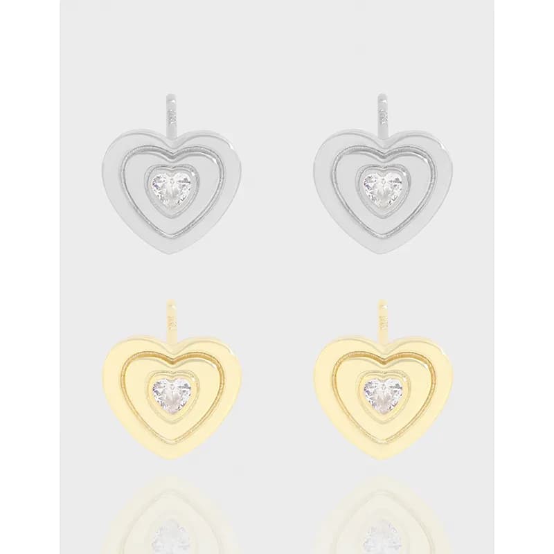 Polished double heart outline earrings with a central clear stone on a light background.
