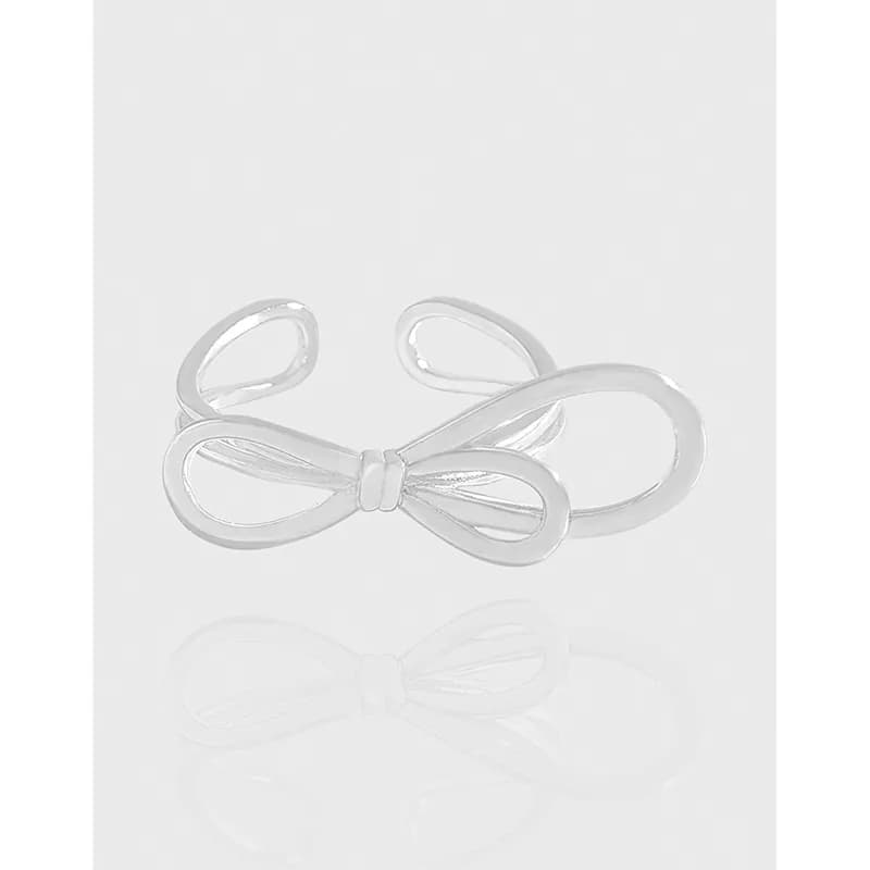 Polished sterling silver bow-shaped ring resting on a white surface, showcasing its reflective curves.