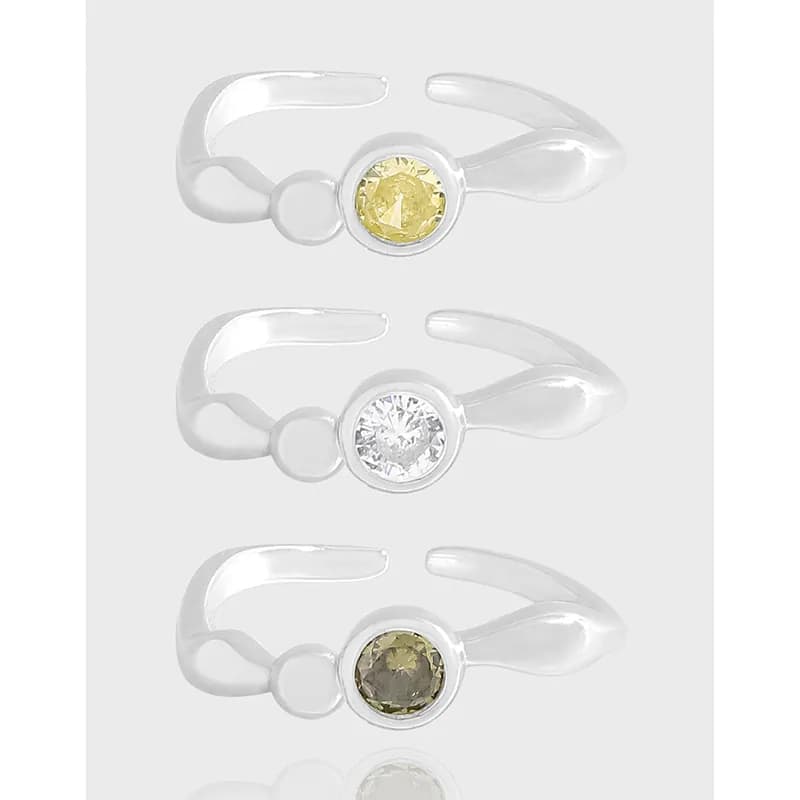 Three sterling silver rings with bezel-set round gemstones on an open, adjustable band