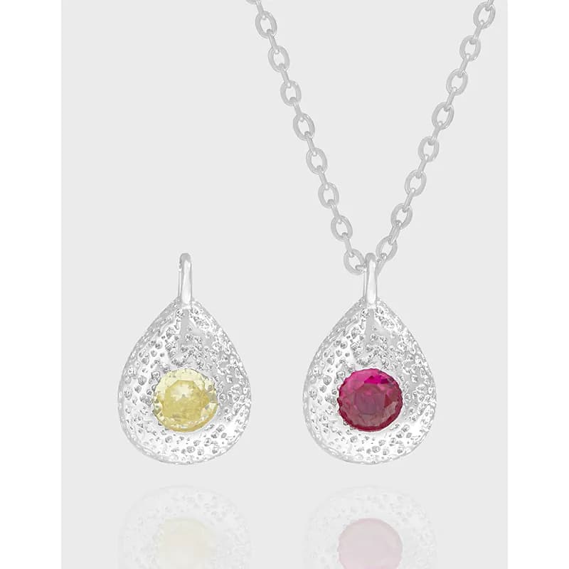 Two teardrop pendants with dotted texture and colored stones on a silver chain.