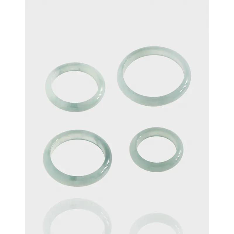 Four polished pale green agate band rings in varying sizes arranged on a white background.