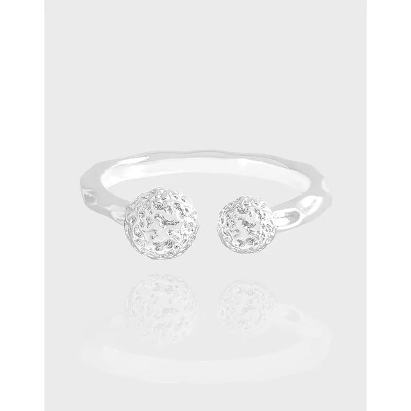 Open-ended sterling silver ring with two textured lattice ball ends on a pale backdrop.