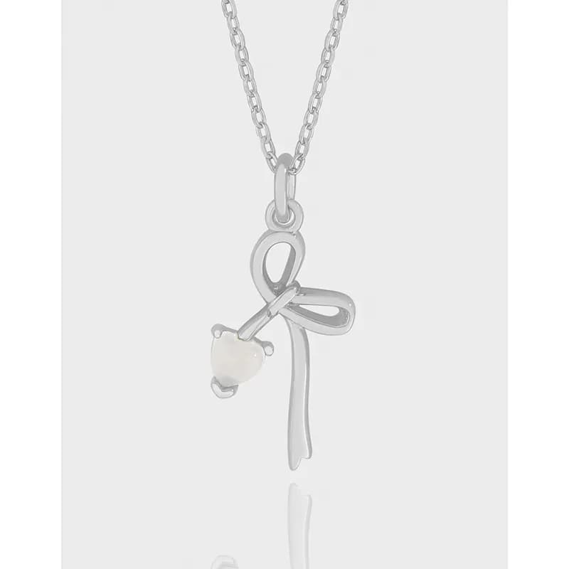 Polished sterling silver ribbon bow pendant on a chain with a small heart gemstone