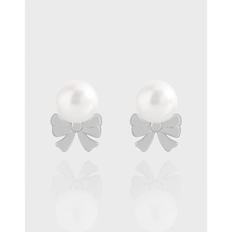 Stud earrings with a white pearl above a polished silver bow motif