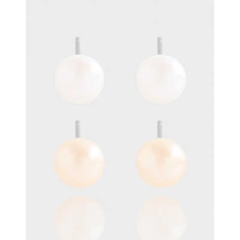 Pair of round white pearl stud earrings on silver posts against a light gray background.