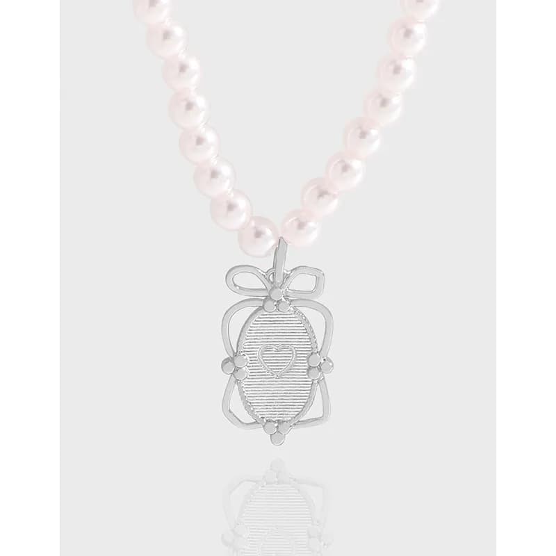 Pearl necklace with a polished silver heart-centered pendant on a pale pink bead chain