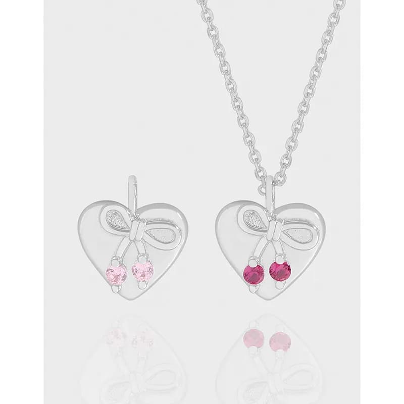 Two polished sterling silver heart pendants with bow motifs and pink gemstone dangles on a delicate chain.