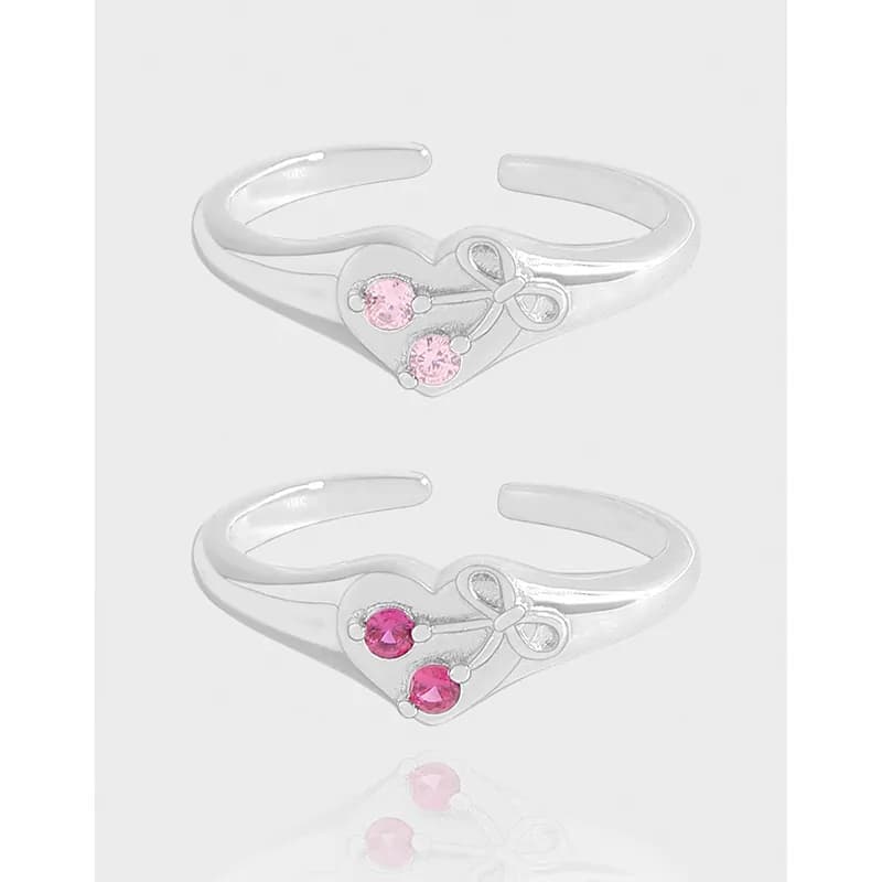 Open-ended sterling silver ring with a heart centerpiece and pink stones on a light background.