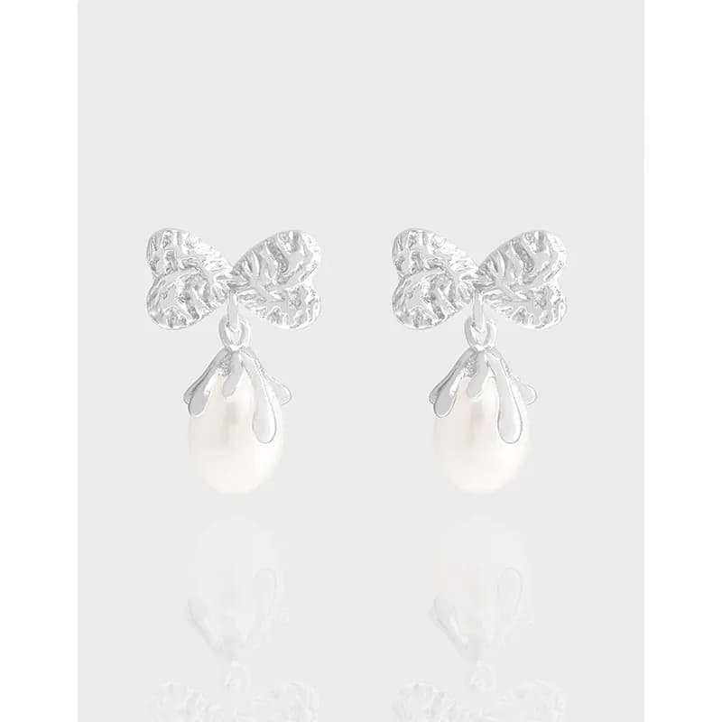 Polished sterling silver bow-shaped top with a pearl drop earrings against a light background.