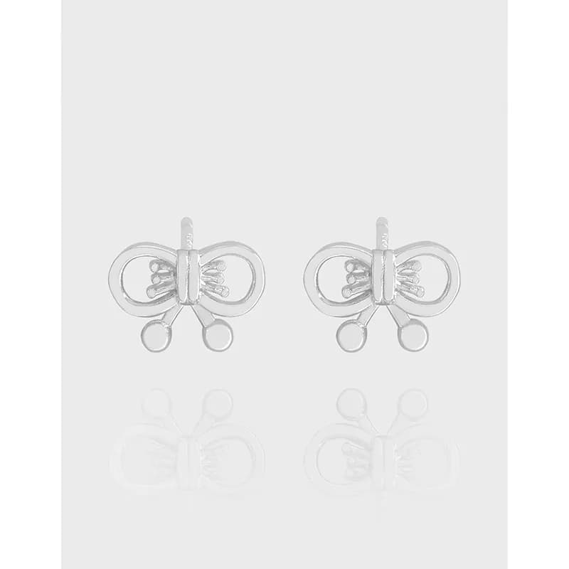 Polished sterling silver bow motif earrings with small dangling circles on a pale background.