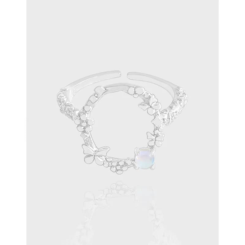 Open silver ring with butterfly and floral charms, featuring a pale opalescent gemstone