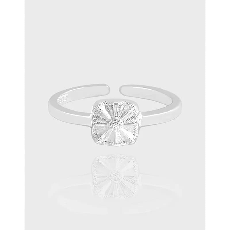 Polished sterling silver ring with a square sunburst bezel on a reflective surface.