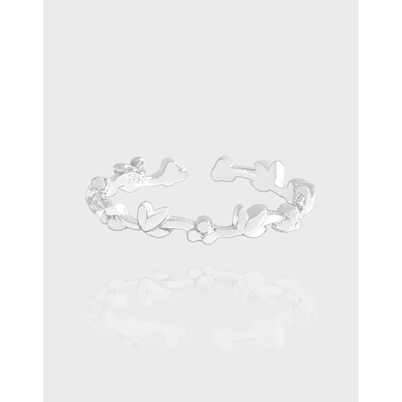 Polished sterling silver ring with heart and petal motifs on a white reflective surface.