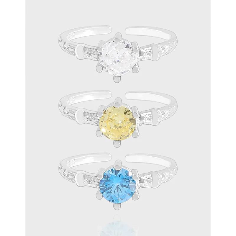 Polished sterling silver round solitaire rings shown in colorless, yellow, and blue stones.