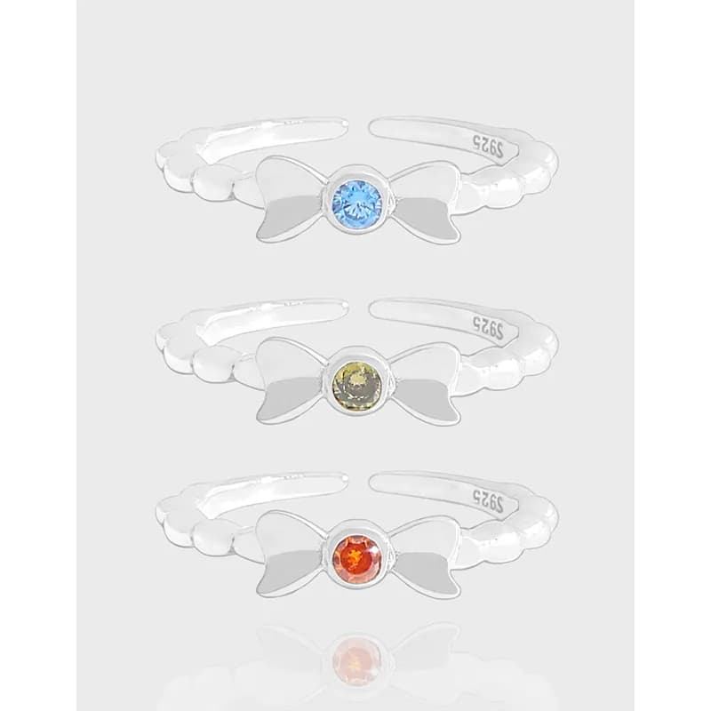 Three sterling silver bow rings with colored bezel stones in blue, yellow, and orange